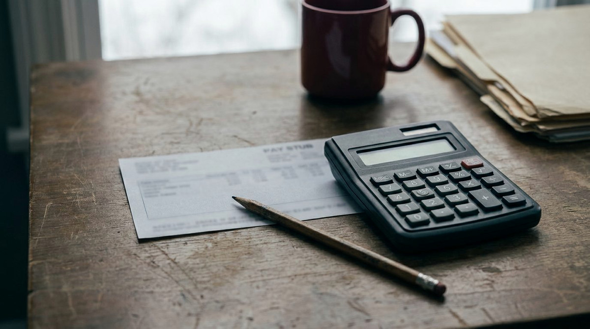 A pay stub next to a desk calculator and a pencil
